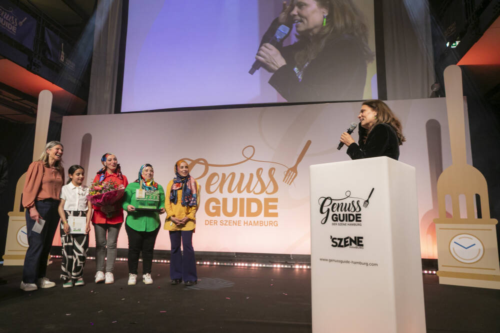 Sarah Wiener hält die Laudatio auf Manuela Maurer und die Köchinnen von Chickpeace / ©Jan-Rasmus Lippels