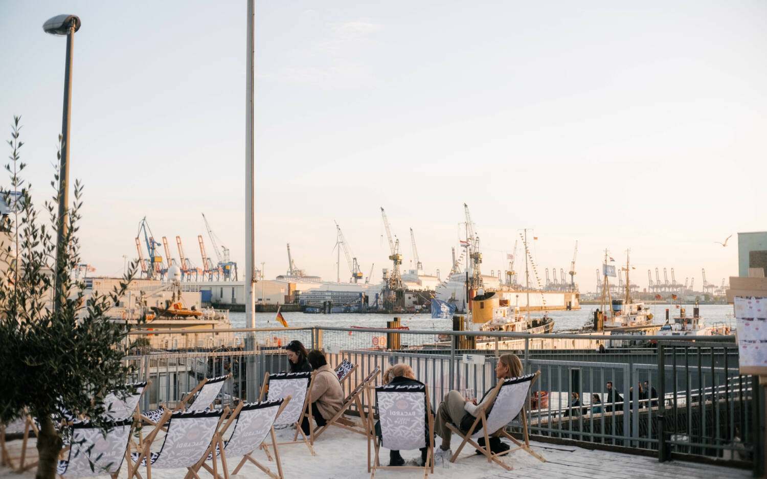 Vom Sonnendeck St. Pauli blickt man auf Wasser, Kräne und untergehende Sonne / ©Lea Harms