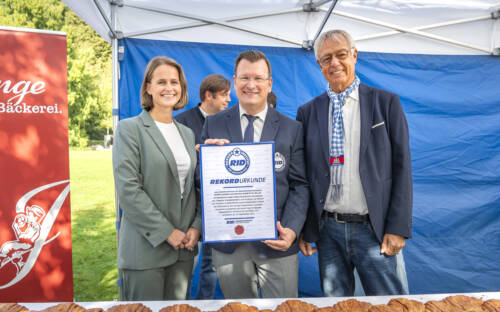 Budnikowsky und Junge Bäckerei feiern Weltrekord mit längstem Franzbrötchen der Welt (v.l.n.r.): Isabelle Junge, Rekordrichter Olaf Kuchenbecker und Cord Wöhlke / ©Budni, Ulrich Schaarschmidt