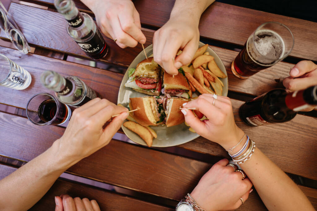 Ein geviertelter Burger wird von 4 Personen geteilt vom Teller genommen.