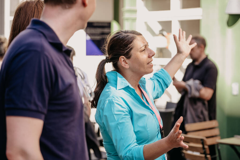 Eine Frau präsentiert zwei zuhörenden etwas mit ausladender Geste.