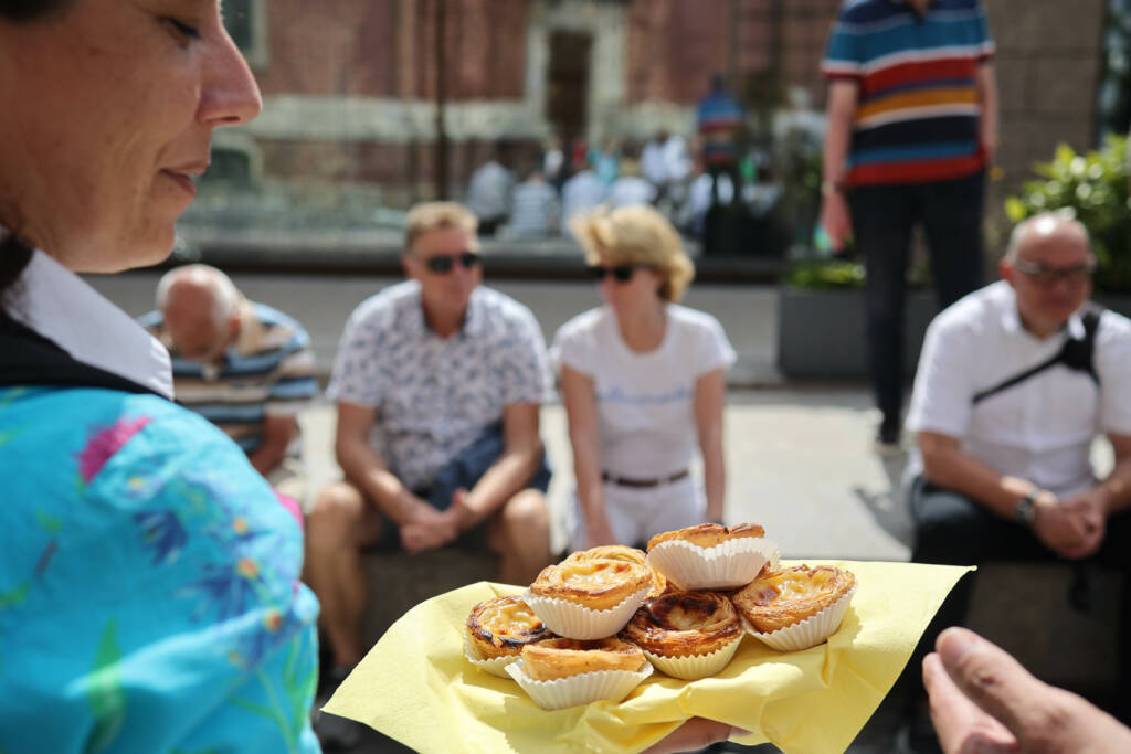 Eine Frau mit einem Tablette Pastel de Nata vor einer sitzenden Gruppe