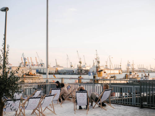 Vom Sonnendeck St. Pauli blickt man auf Wasser, Kräne und untergehende Sonne / ©Lea Harms