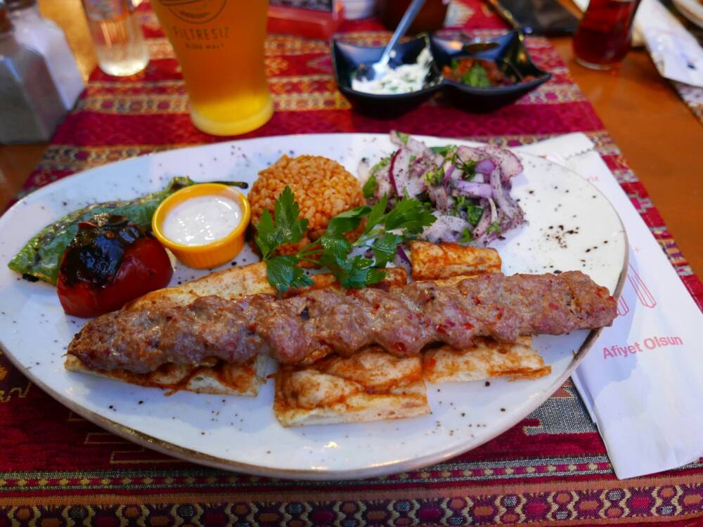 Herzhaft, würzig, richtig schön vom Grill, Adana Kebap kommt hier mit Bulgur, gegrilltem Gemüse, Zwiebeln und Joghurt auf den Tisch / ©Unsplash/Vitaly Mazur